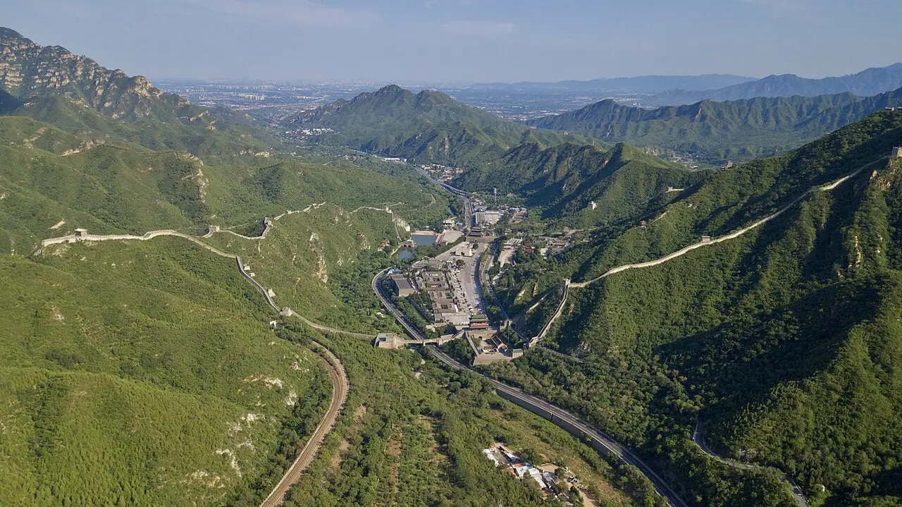 A muralha em linha clara sobre as cristas verdes e uma estrada no fundo do vale.