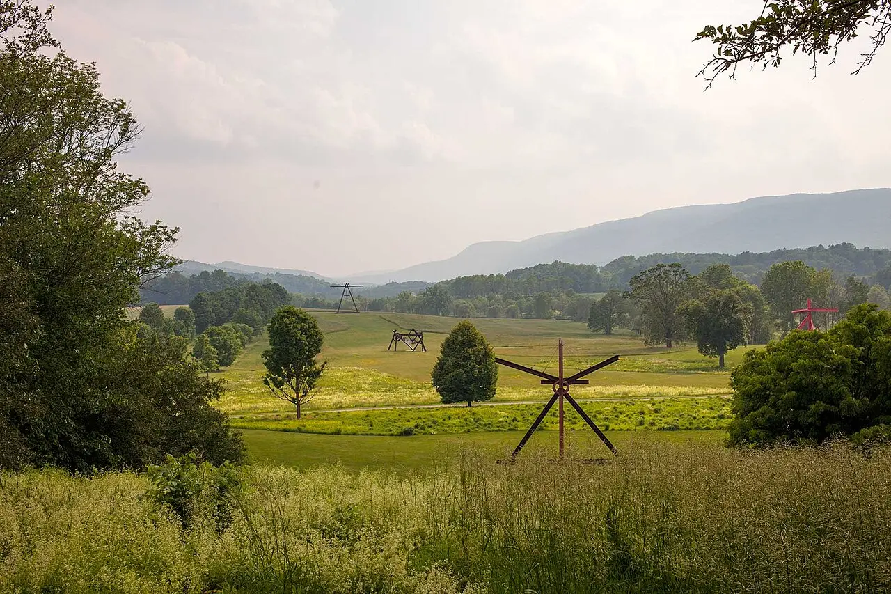 Campo aberto com esculturas de aço de grande porte, uma delas vermelha, entre árvores e prados, com montanhas azuladas ao fundo, no Storm King Art Center.