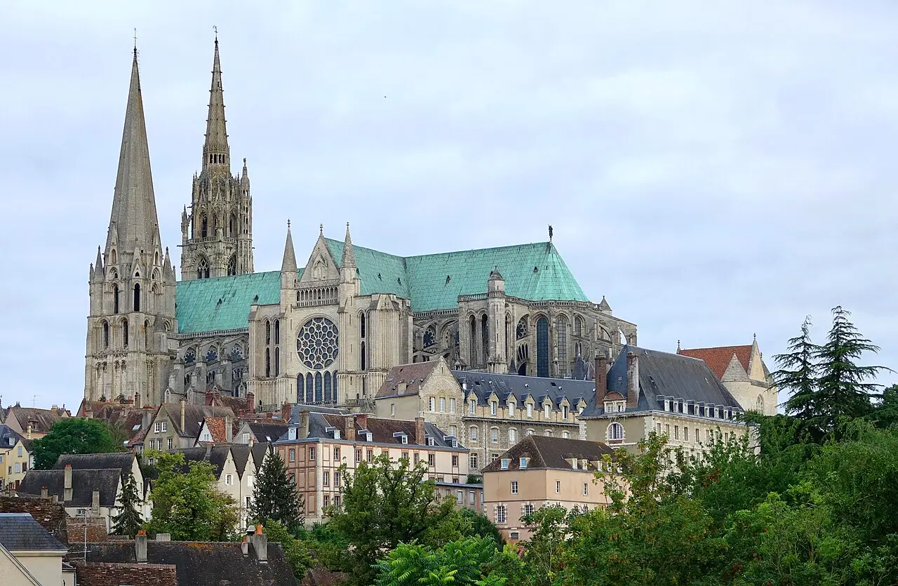La catedral de Chartres sobre la ciudad, con dos torres de agujas desiguales, tejado de cobre verdoso y casas antiguas en primer plano.