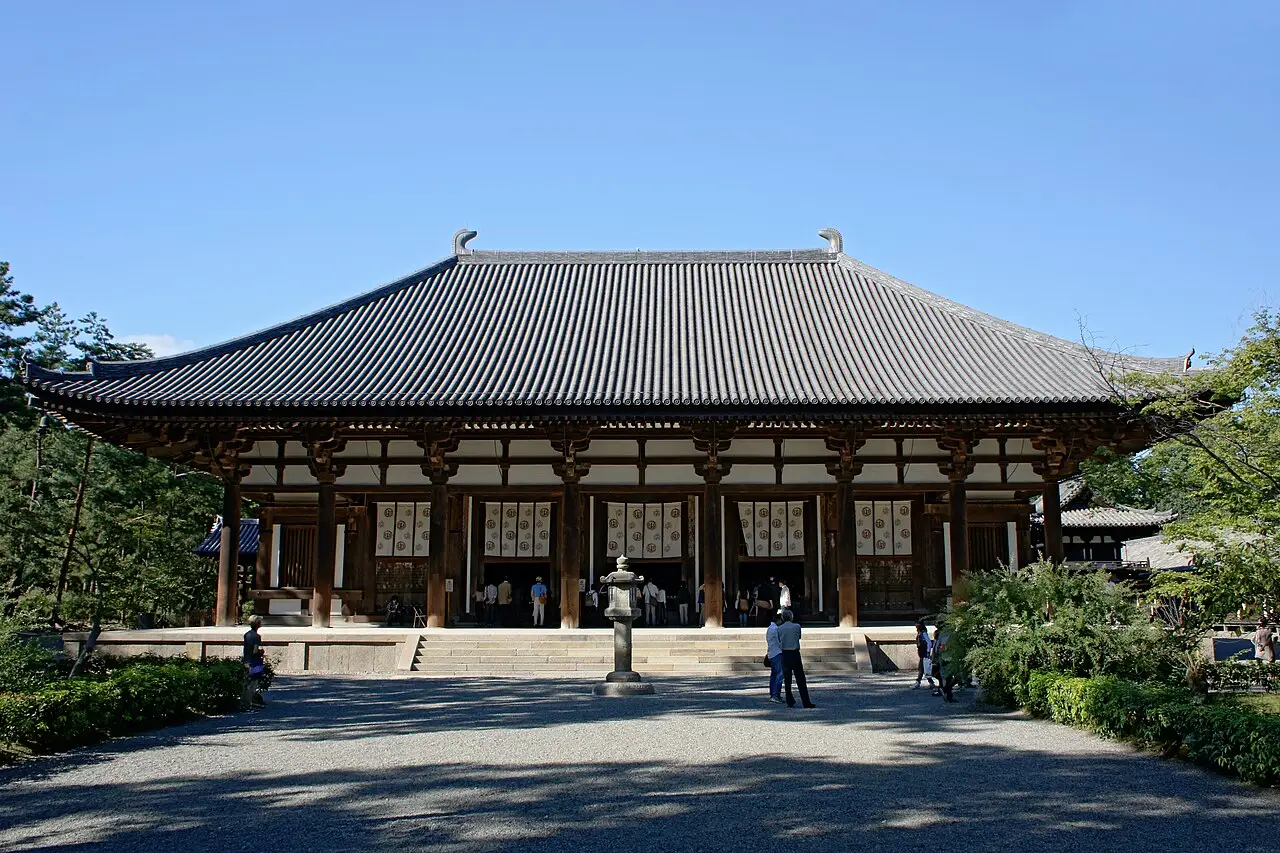 O pavilhão principal do templo Tōshōdai-ji, em Nara, de madeira com telhado largo de telhas cinza, uma lanterna de pedra na frente e visitantes no pátio.
