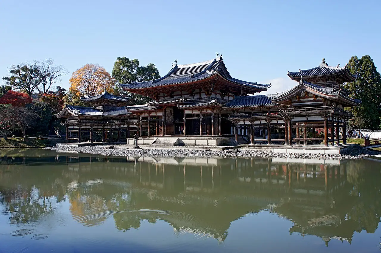 O Pavilhão da Fênix do Byōdō-in, em Uji, de madeira com telhados de telha escura, refletido na água do lago, com árvores de outono ao fundo.