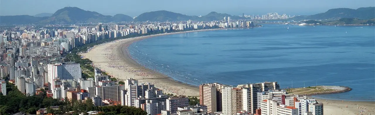 Orla em curva, com a praia, a fileira de prédios e os morros ao fundo.