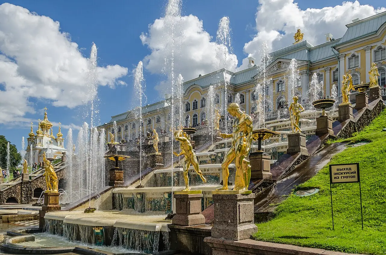 A Grande Cascata de Peterhof, com estátuas douradas ao longo dos degraus, jatos de água em primeiro plano e o palácio amarelo ao fundo.