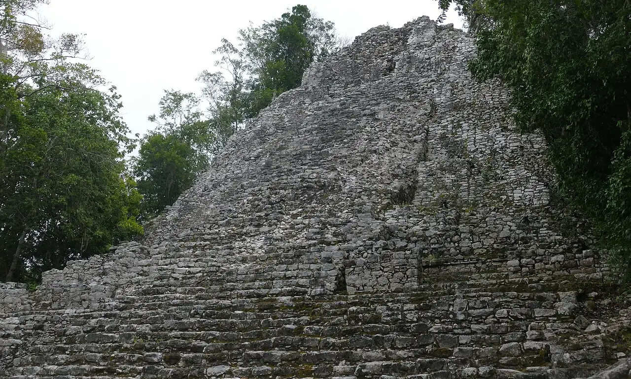 Escadaria de blocos de pedra cinza da pirâmide de Cobá, subindo até o alto entre árvores da selva dos dois lados.