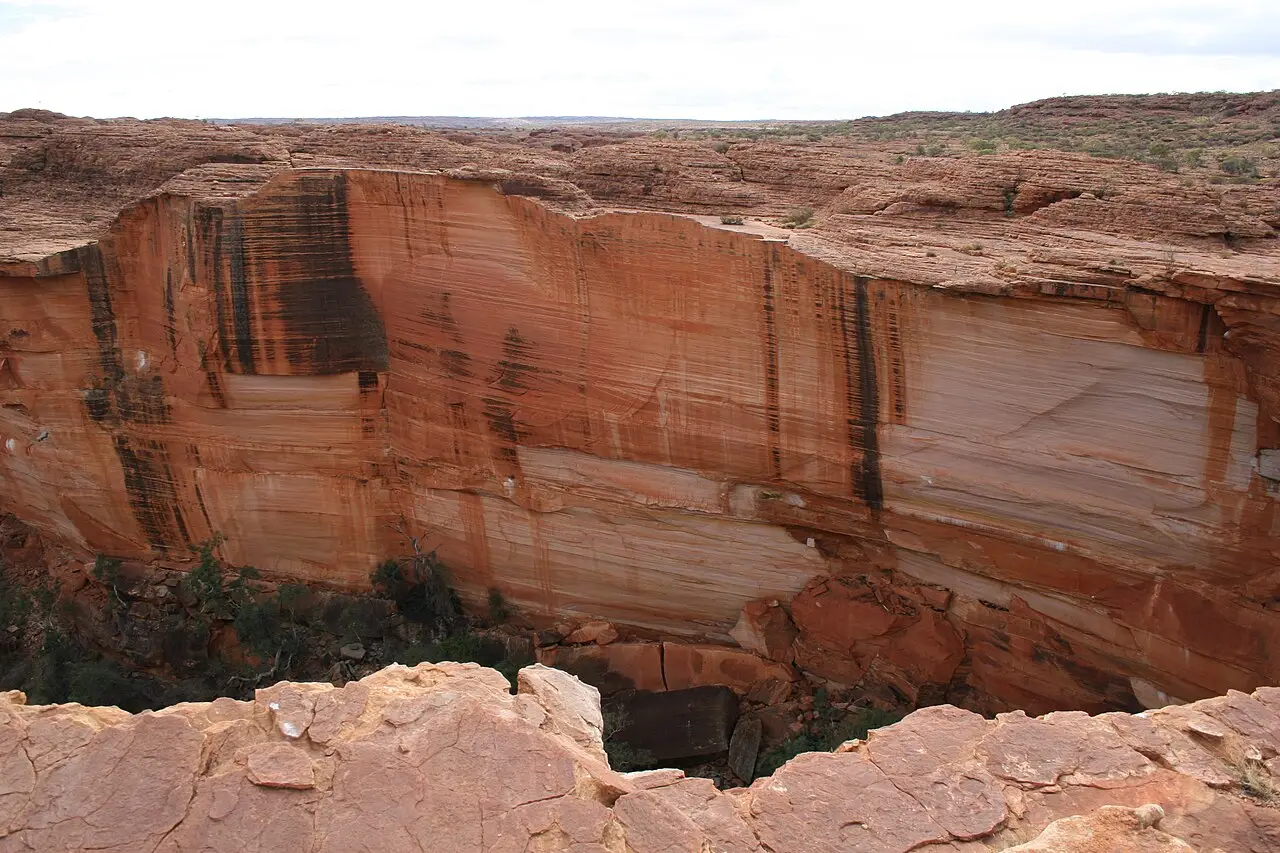 Paredão de arenito vermelho e cor de creme, com faixas escuras de manchas de água, caindo num desfiladeiro visto da borda, em Kings Canyon.