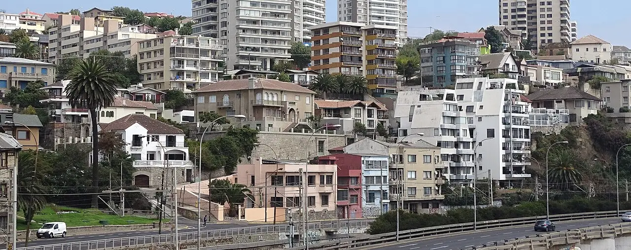 Prédios de apartamentos e casas nas encostas de um bairro de Viña del Mar, com palmeiras entre eles e uma via expressa na parte de baixo.
