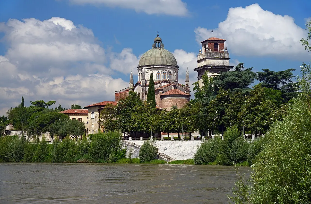 A igreja de São Jorge em Braida, com cúpula verde e campanário de tijolo, entre árvores na margem do rio Adige, em Verona.