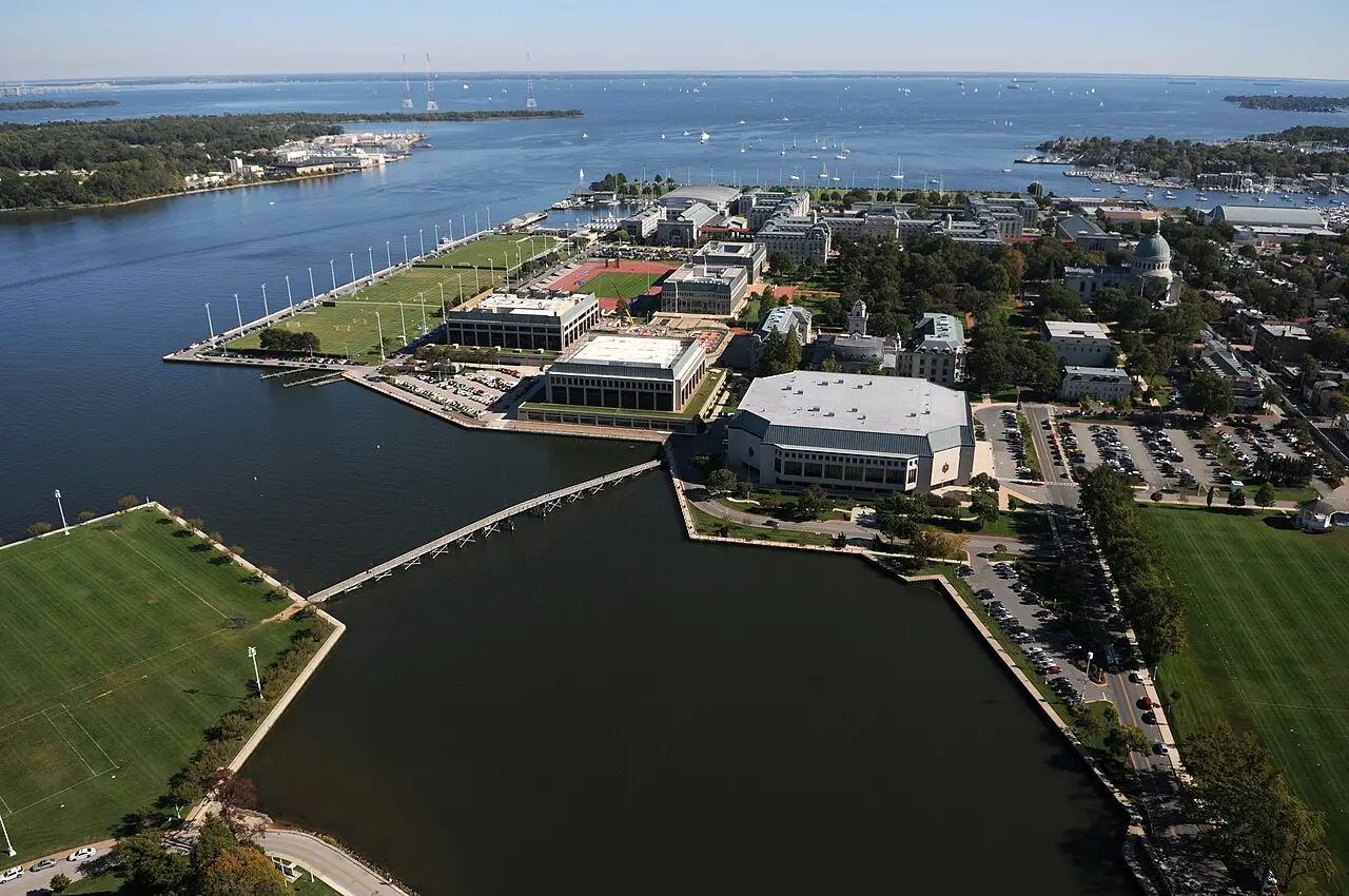 Vue aérienne de l’Académie navale des États-Unis, à Annapolis, avec des bâtiments parmi des terrains verts et un bassin sombre au premier plan.