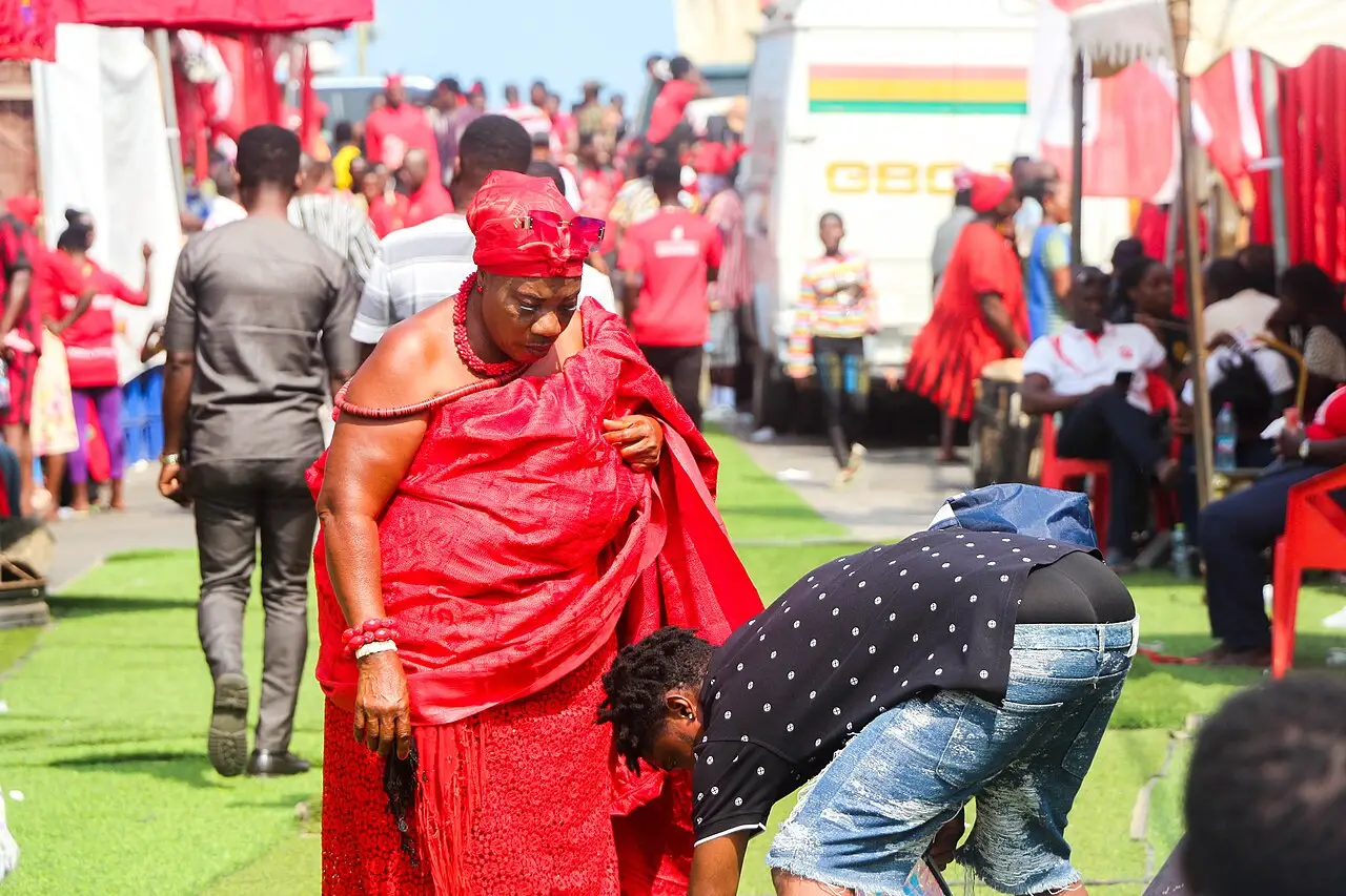 Des personnes vêtues de rouge, en pagnes traditionnels, sont réunies sur un terrain ouvert avec des tentes et des drapeaux rouges pendant le Homowo à Accra.