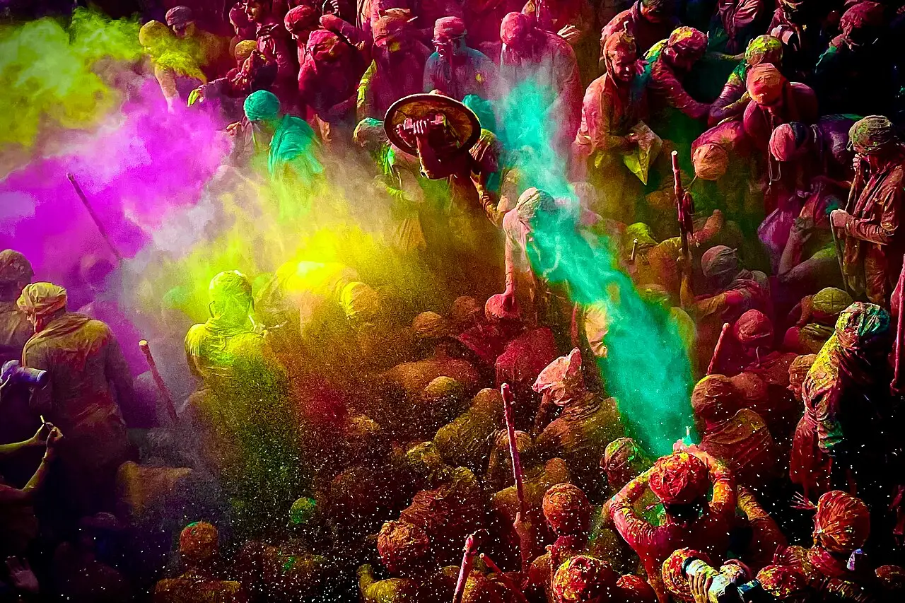 Multidão coberta de pó colorido em rosa, verde e amarelo durante o Holi em Nandgaon, na região de Mathura.