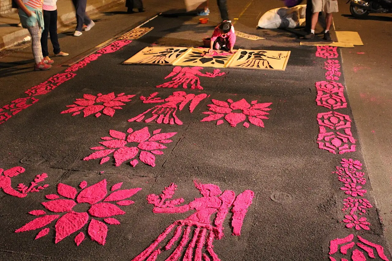 Tapete de serragem com desenhos de flores rosa sendo feito na rua à noite, antes de uma procissão em Antigua.