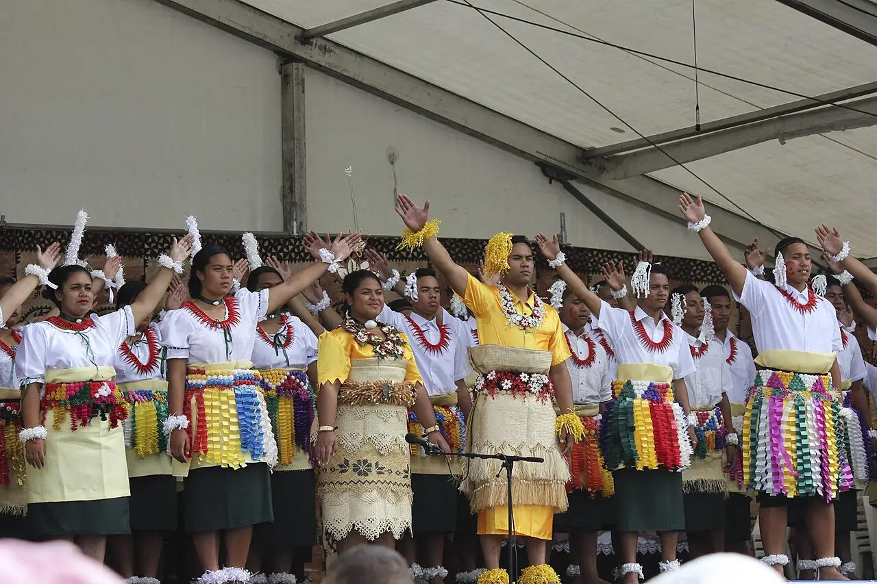 Grupo de dançarinos com saias de fibra e colares de flores fazendo a dança lakalaka tonganesa sob uma tenda no ASB Polyfest.