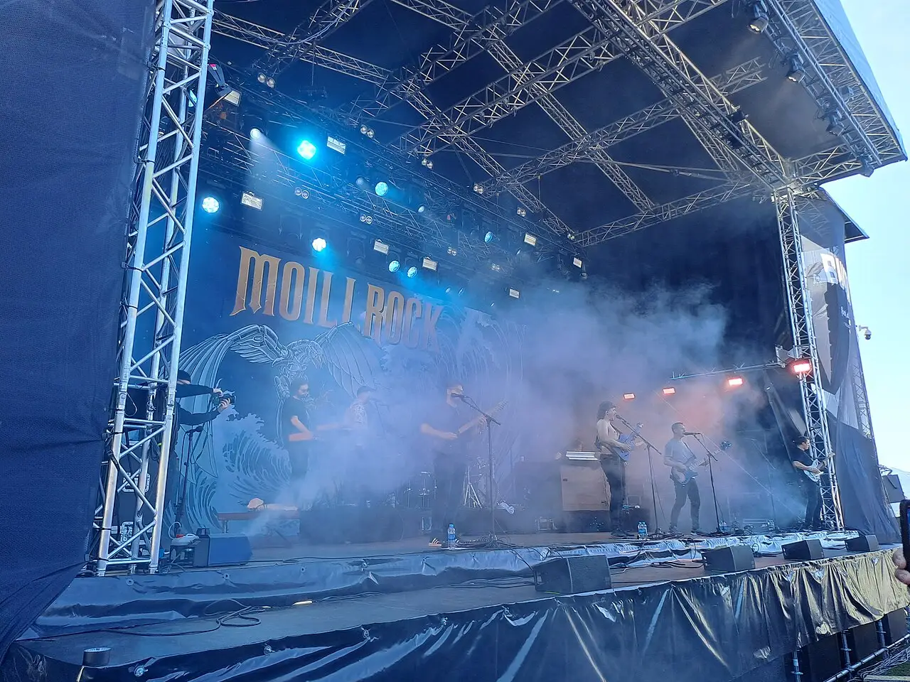 Palco com estrutura metálica, fumaça e luzes azuis diante da plateia no festival Bukta Tromsø Open Air, com céu claro ao fundo.