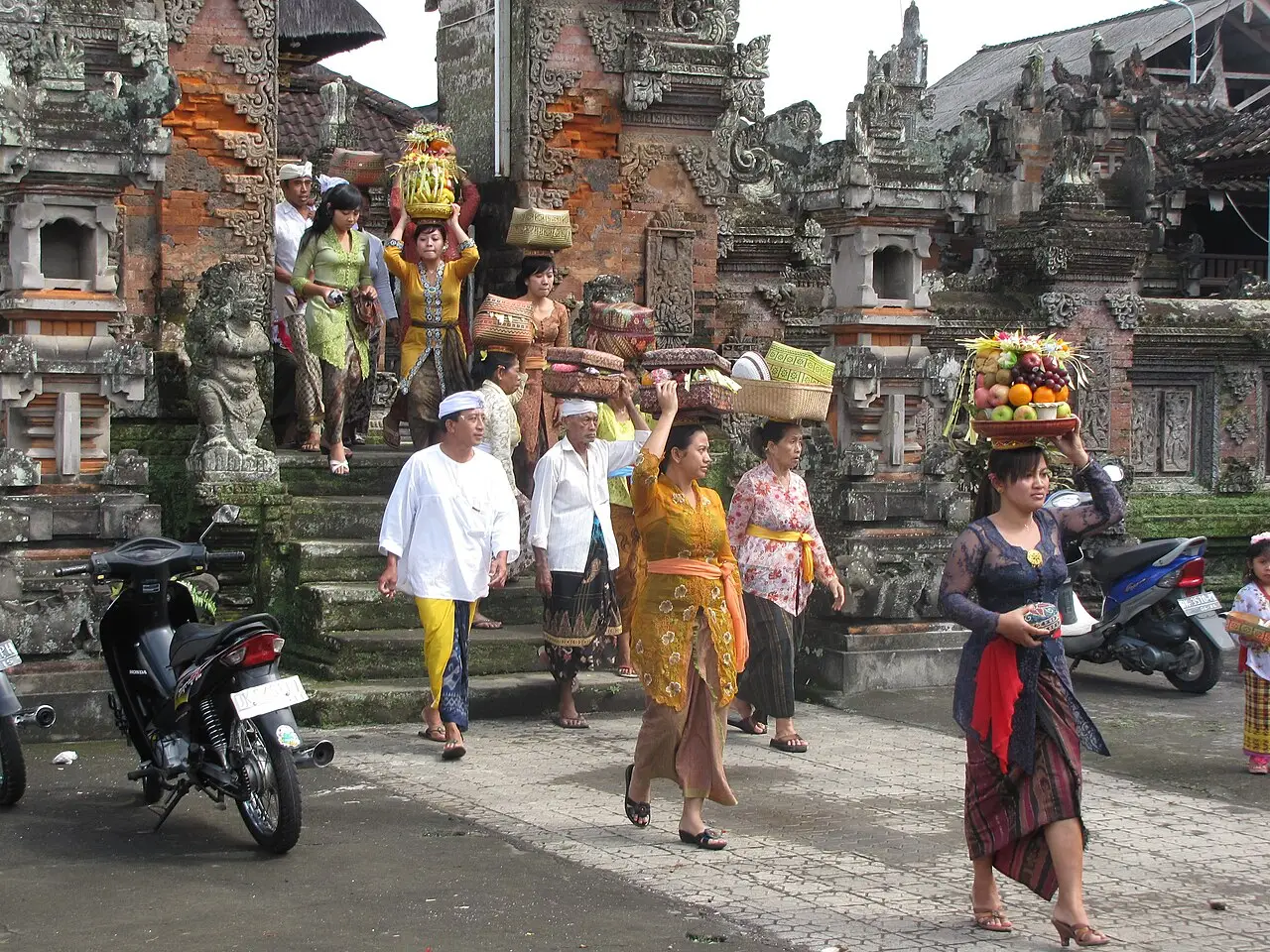 Mulheres em trajes tradicionais carregam oferendas na cabeça e descem os degraus de um templo balinês durante o Kuningan.