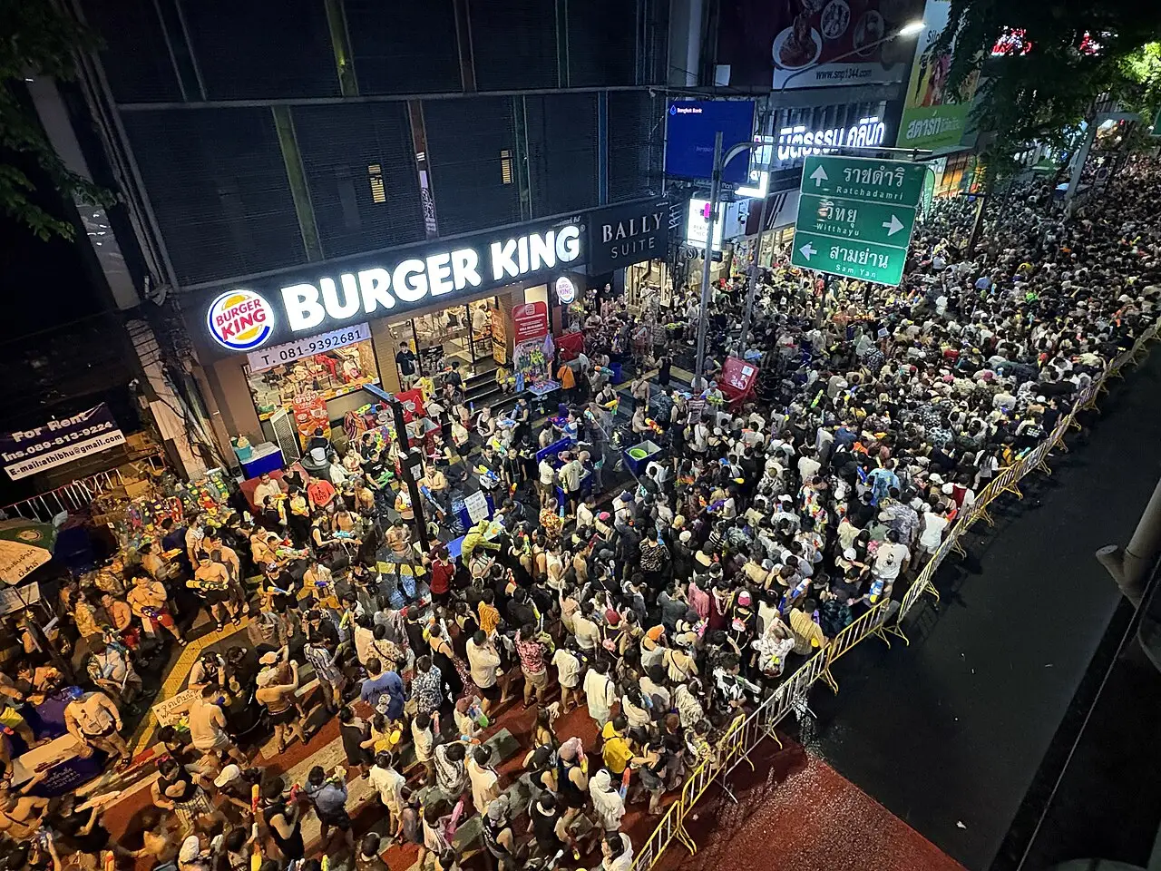 Multidão densa vista de cima na Rua Si Lom, em Bangkok, durante o Songkran de 14 de abril de 2025, à noite.