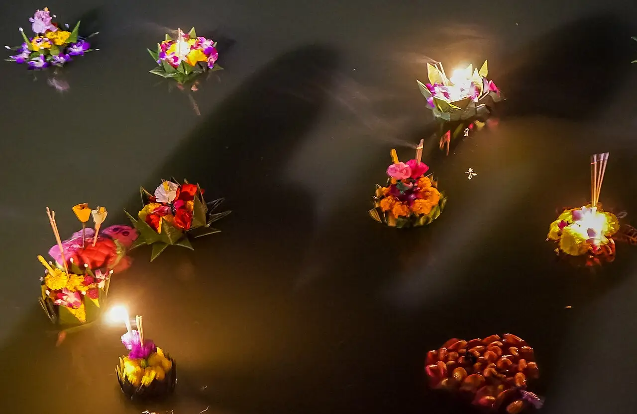 Krathongs decorados com flores e velas acesas flutuam na água escura durante o Loi Krathong, em Bangkok.