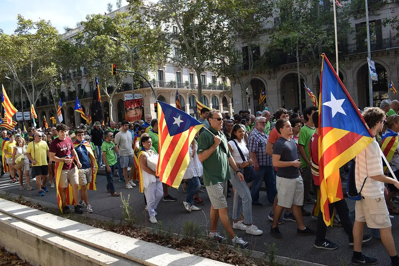 Manifestantes caminham por uma avenida arborizada com bandeiras estreladas catalãs na Diada Nacional de Catalunya de 2024, em Barcelona.