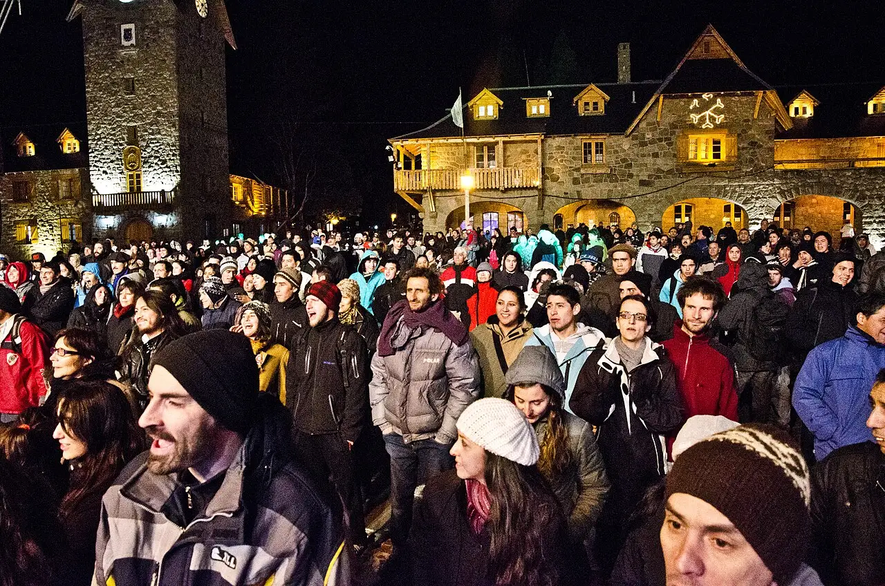 Multidão agasalhada à noite diante de edifícios de pedra iluminados, na Fiesta Nacional de la Nieve de 2014, em Bariloche.