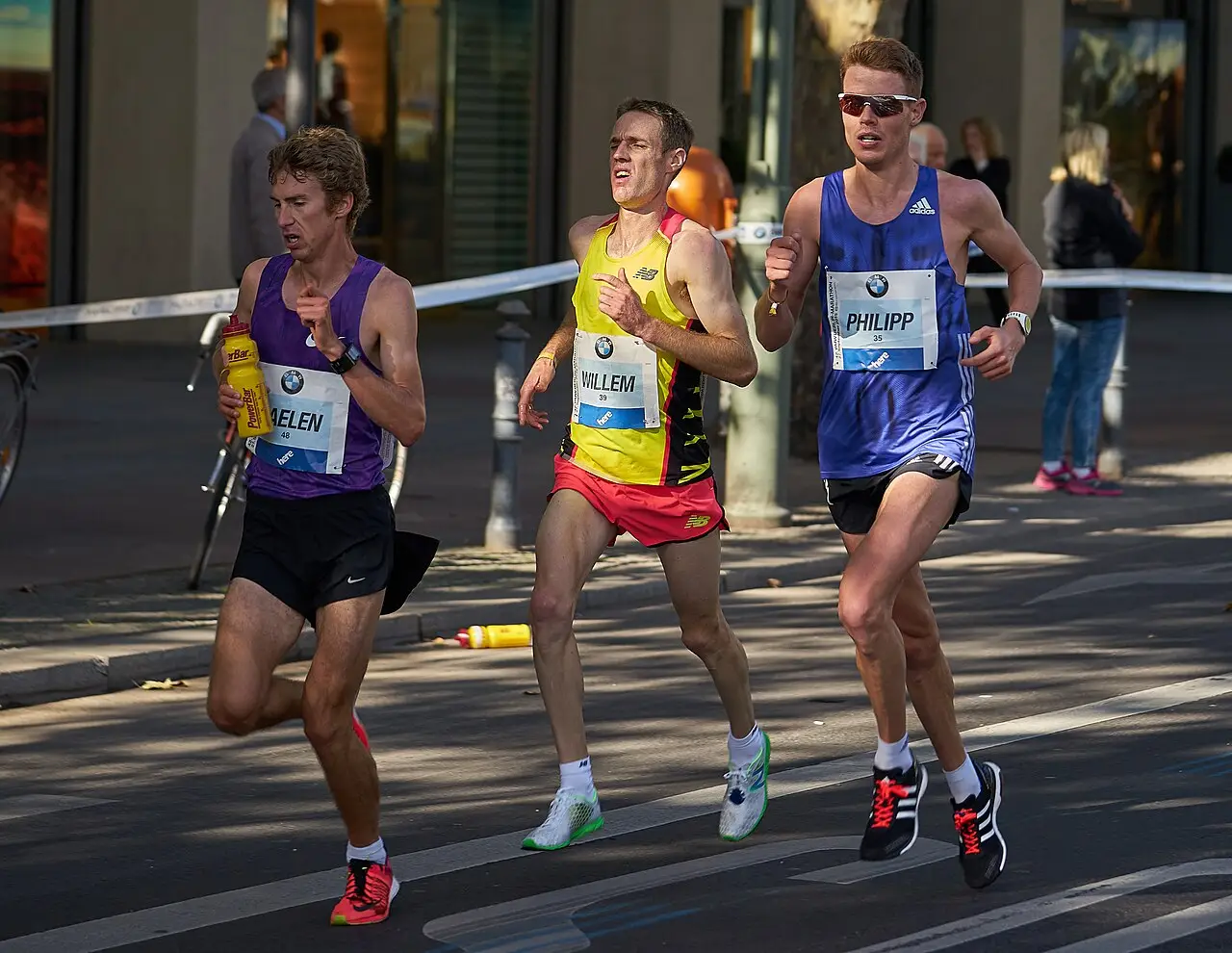 Três corredores com números de peito passam por uma rua de Berlim na Maratona de Berlim de 2015.