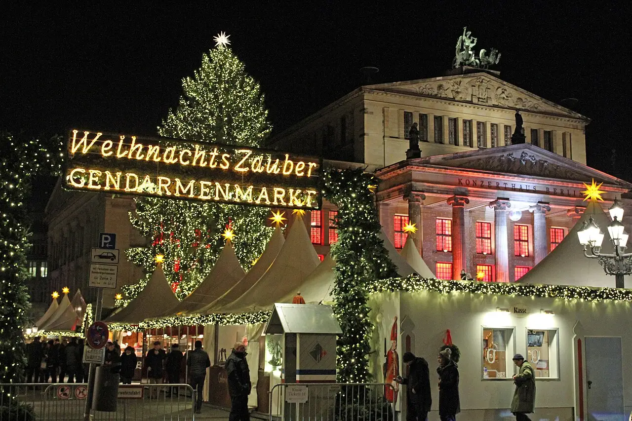 Mercado de Natal Weihnachtszauber na Gendarmenmarkt, em Berlim, à noite, com árvore de Natal e barracas iluminadas diante do edifício.