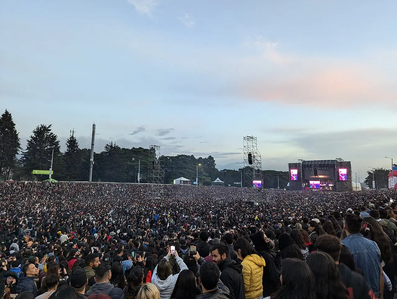 Multidão enorme diante de um palco distante em um parque ao entardecer, no Rock al Parque de 2024, em Bogotá.