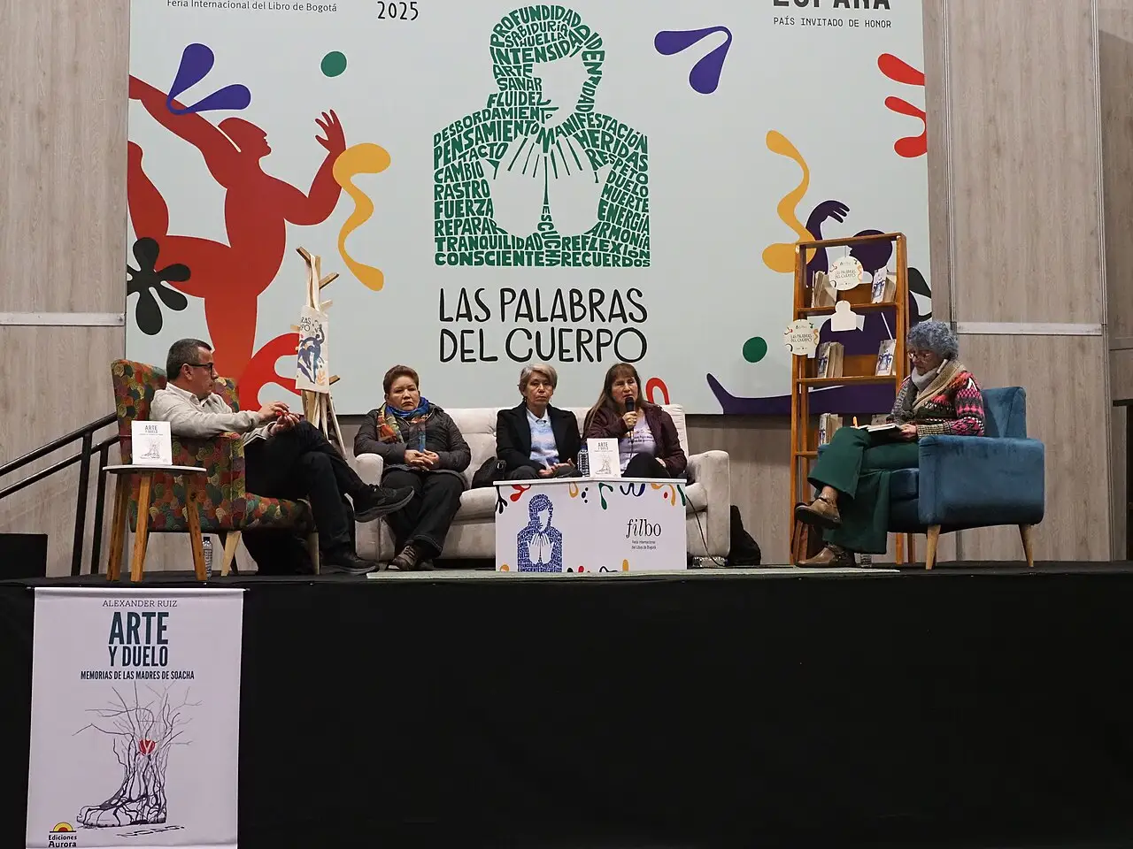 Palco da FILBo de 2025 com um painel de pessoas sentadas diante de um cartaz de cores vivas com o título Las palabras del cuerpo.
