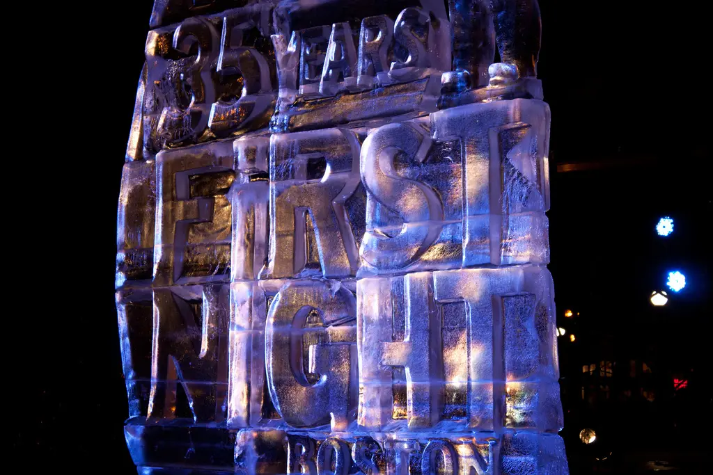 Escultura de hielo con las palabras First Night y 35 Years, iluminada en azul y violeta sobre un fondo oscuro.