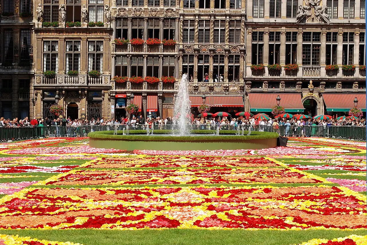 Tapete de flores vermelhas, amarelas e verdes na Grand-Place de Bruxelas, com a fonte e as casas históricas ao fundo, em 2010.