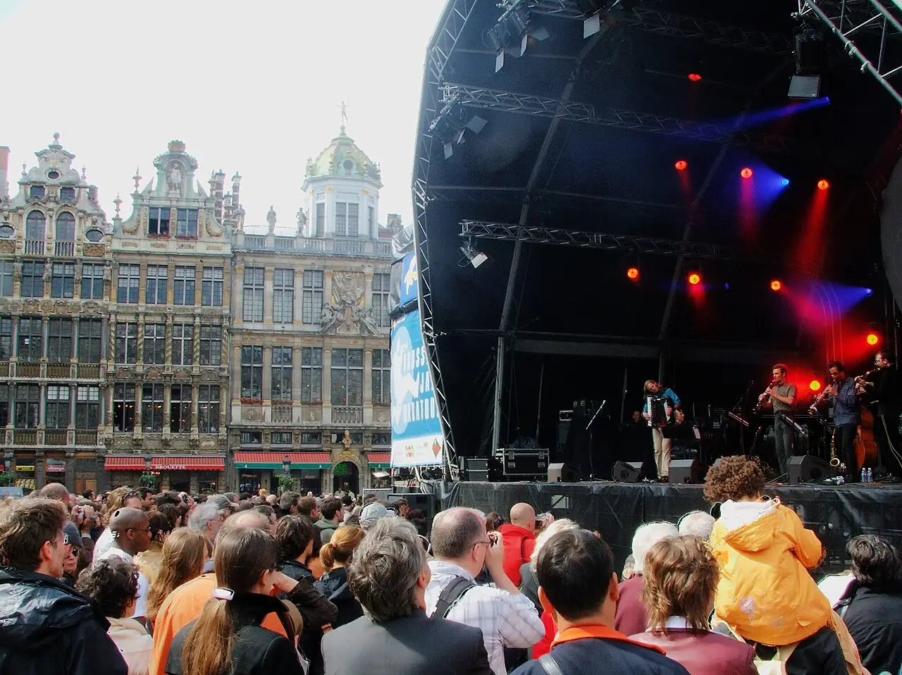 Palco com luzes coloridas montado ao lado das casas históricas da Grand-Place, com público em frente, no Brussels Jazz Marathon.