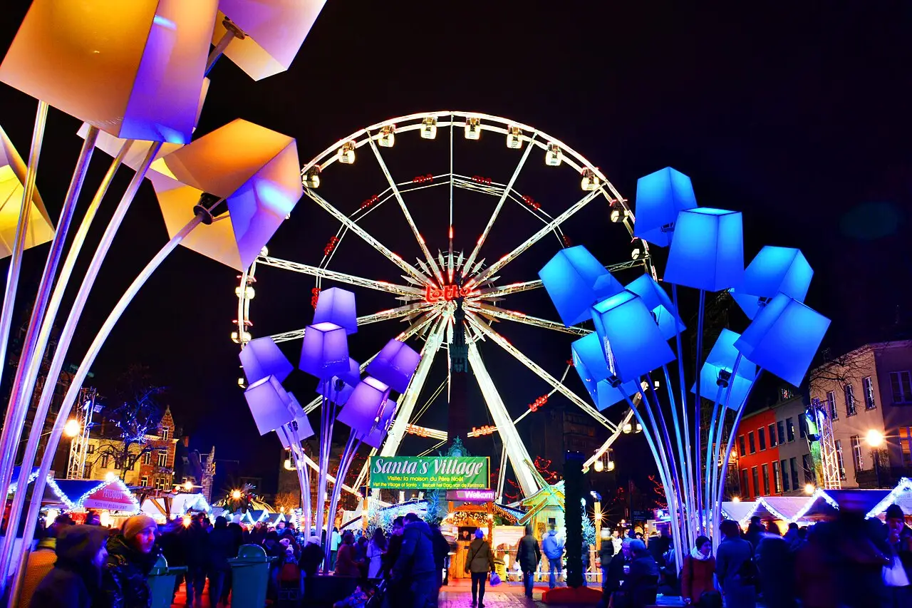 Grande roda-gigante iluminada à noite, com esculturas de flores luminosas e visitantes, no mercado de inverno Plaisirs d’Hiver, em Bruxelas.