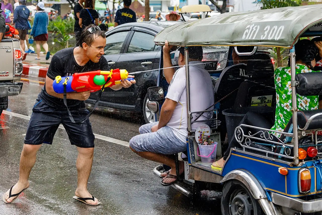 Homem com pistola de água ao lado de um tuk-tuk em uma rua molhada durante o Songkran de 2017, em Chiang Mai.