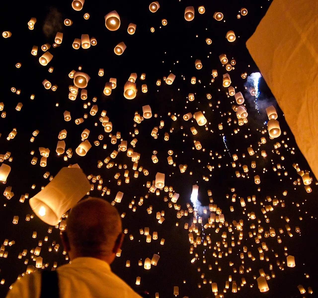 Lanternas de papel iluminadas sobem contra o céu noturno; uma pessoa é vista de costas em primeiro plano, em San Sai.