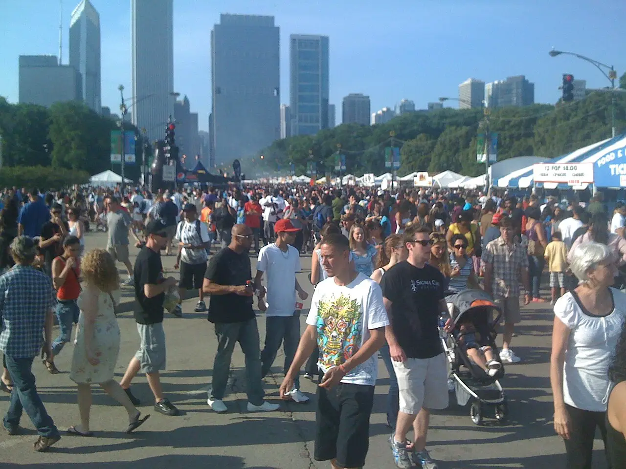 Multidão caminhando entre barracas no Taste of Chicago de 2011, com arranha-céus ao fundo sob céu claro.