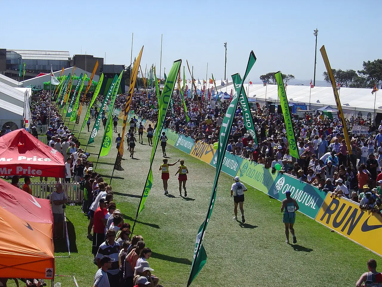 Área de chegada da Two Oceans Marathon com bandeiras verdes ao longo do gramado e público de ambos os lados.