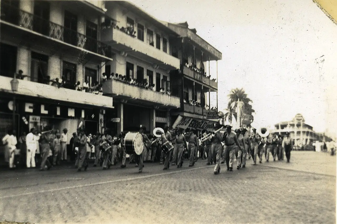 Fotografia antiga de uma banda desfilando em uma rua da Cidade do Panamá durante o Carnaval de 1946, com espectadores nas sacadas.