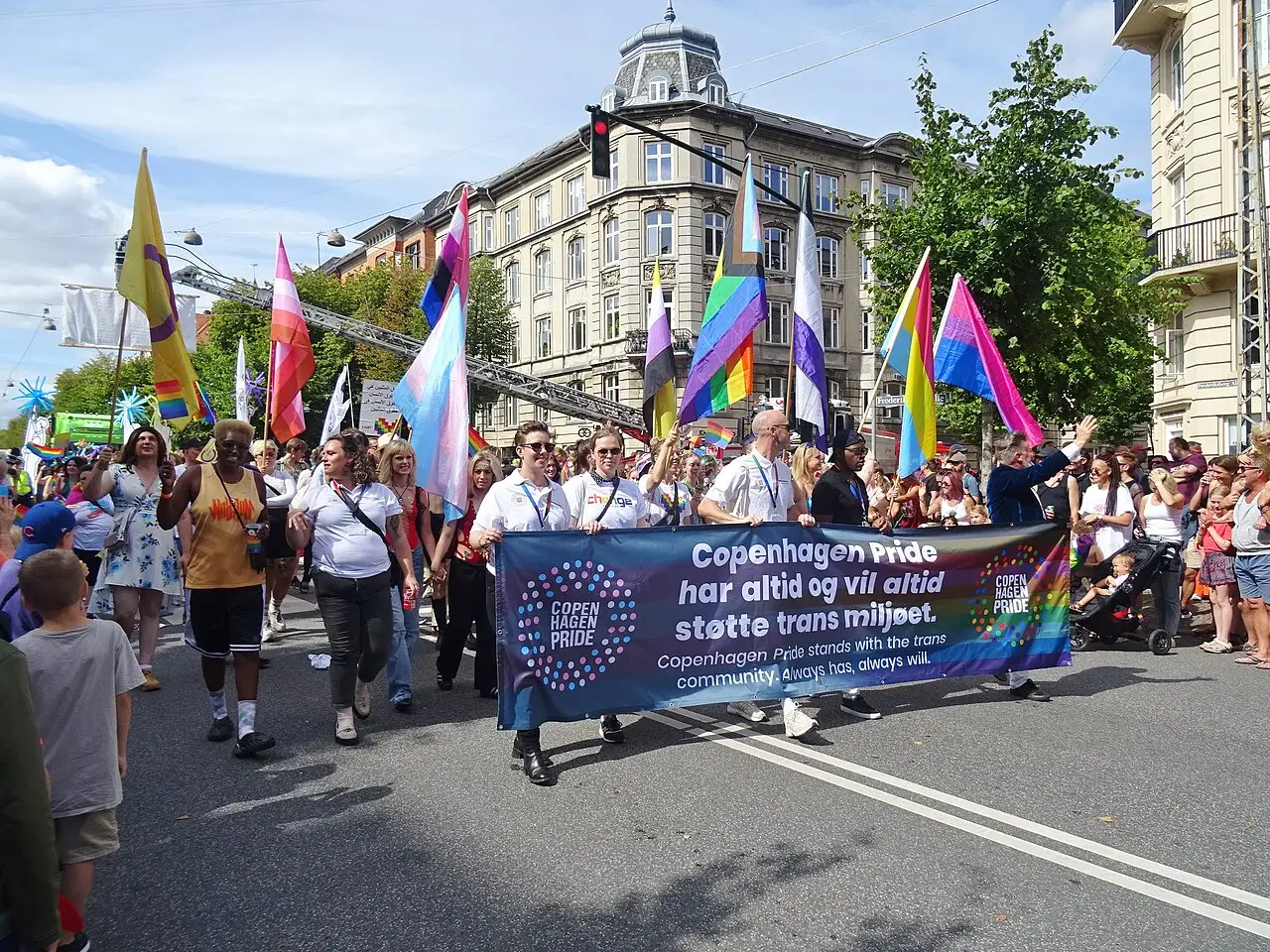 Participantes com bandeiras de arco-íris e uma faixa caminham por uma rua de Copenhague na Copenhagen Pride Parade de 2022.