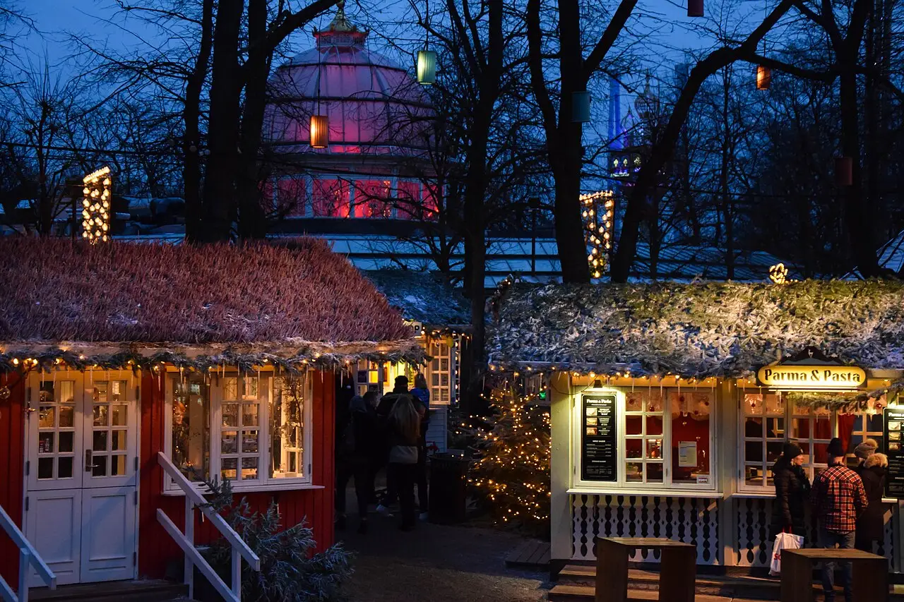 Duas cabanas de madeira do mercado de Natal do Tivoli ao entardecer, com telhados nevados e árvores sem folhas ao redor.