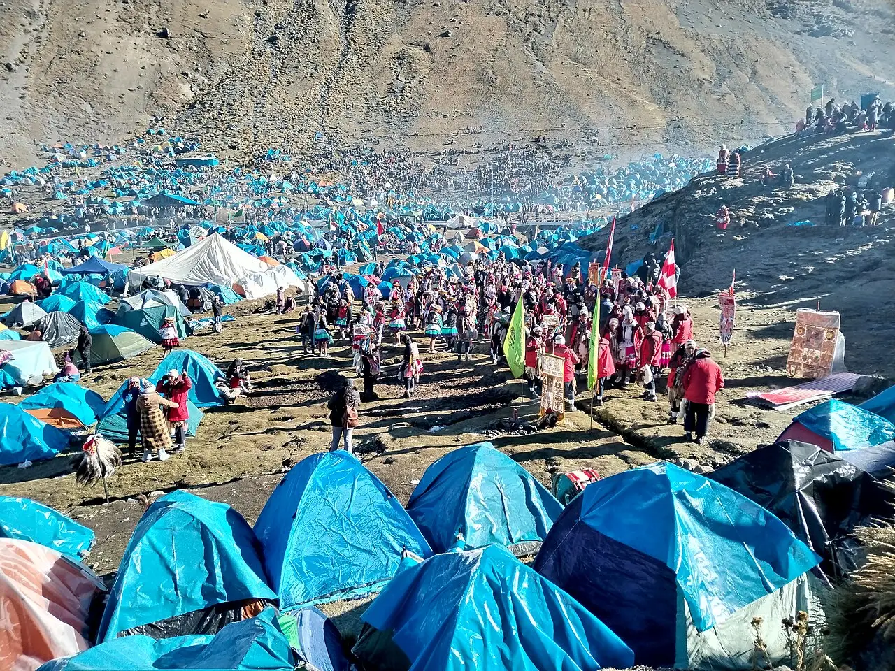 Vale de montanha cheio de barracas azuis e pessoas com trajes coloridos dançando entre elas durante a peregrinação do Qoyllur Rit’i.