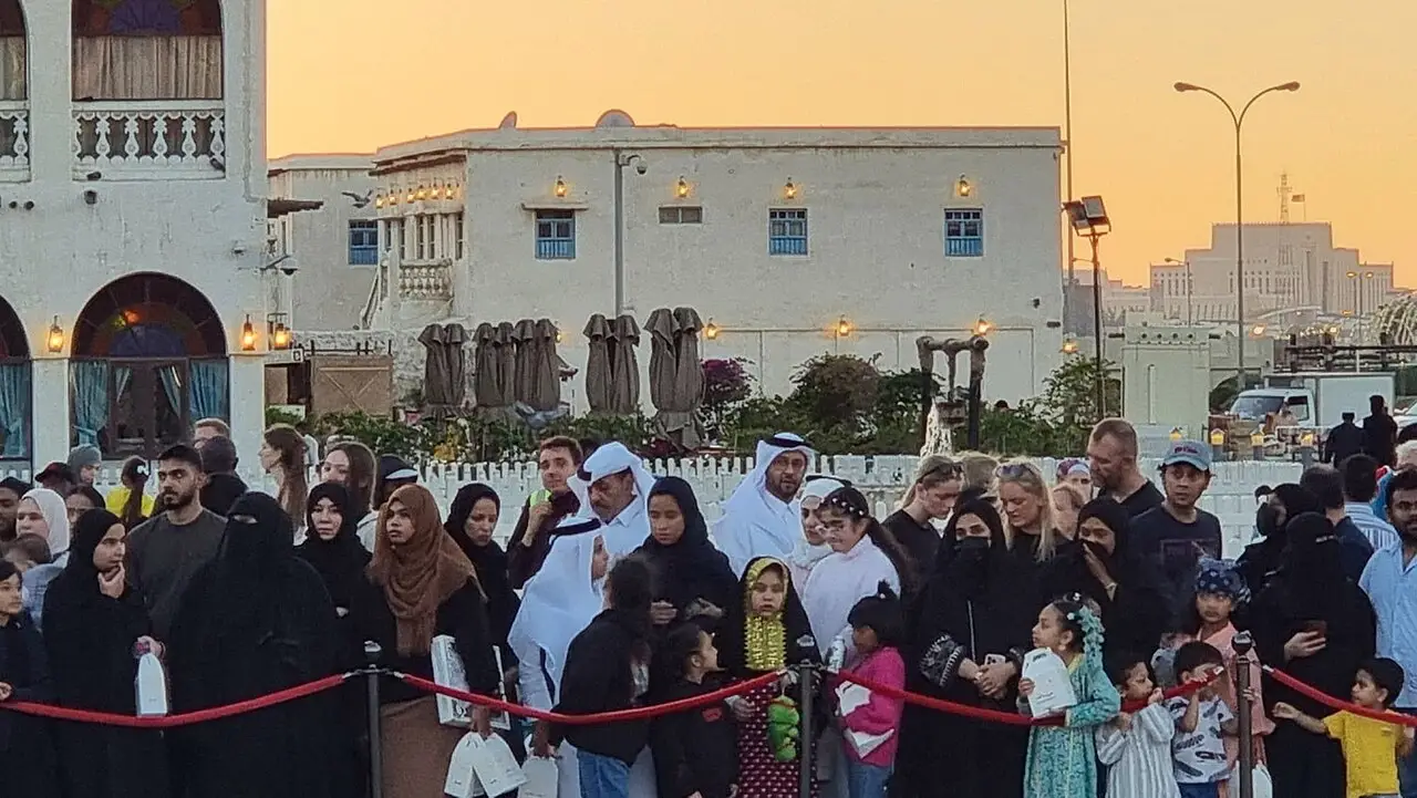 Multidão de homens, mulheres e crianças reunida atrás de uma corda vermelha no Souq Waqif, em Doha, à espera do tiro do canhão do Ramadã.