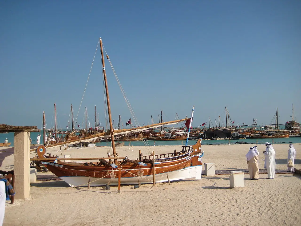 Barcos de madeira encalhados na areia do festival de dhows em Katara, Doha, com homens de branco ao fundo, em 22 de novembro de 2013.