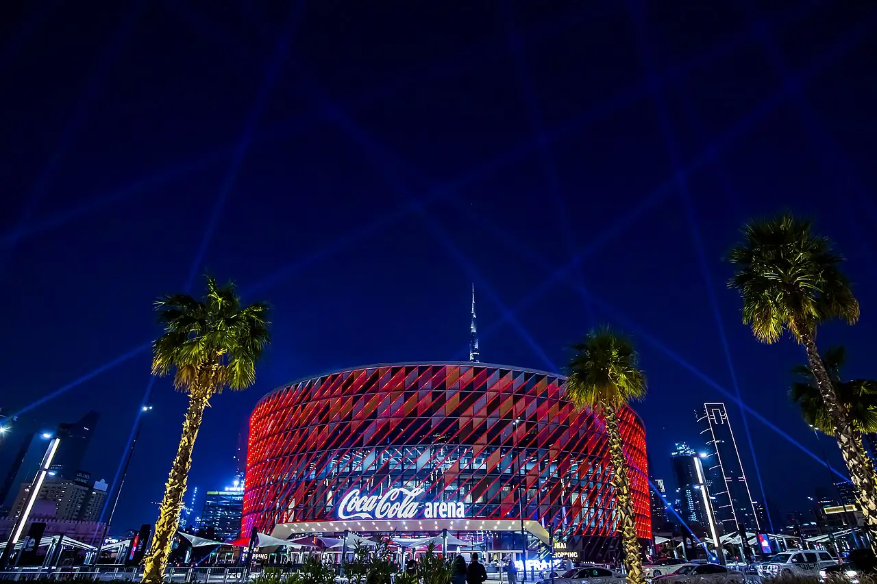 Coca-Cola Arena iluminada em vermelho, com feixes de laser azuis e palmeiras em primeiro plano, durante a celebração de encerramento do festival.