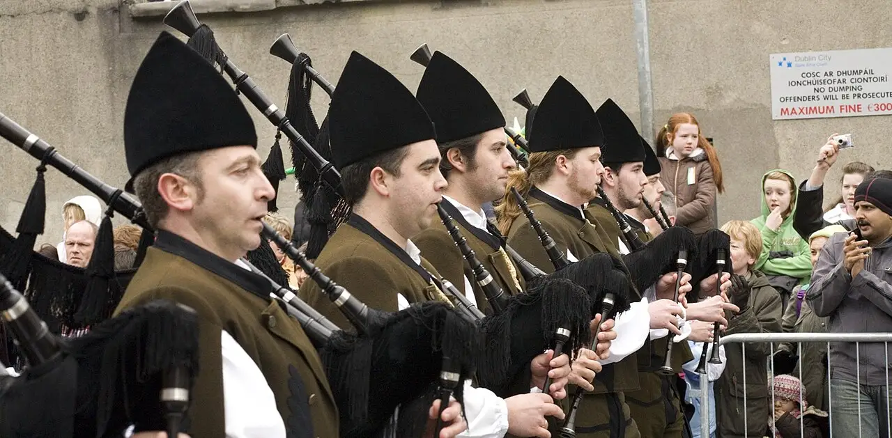 Gaiteiros de gorro preto e casaco escuro tocando durante o St. Patrick’s Festival em Dublin, em 2007, com espectadores atrás de uma grade.