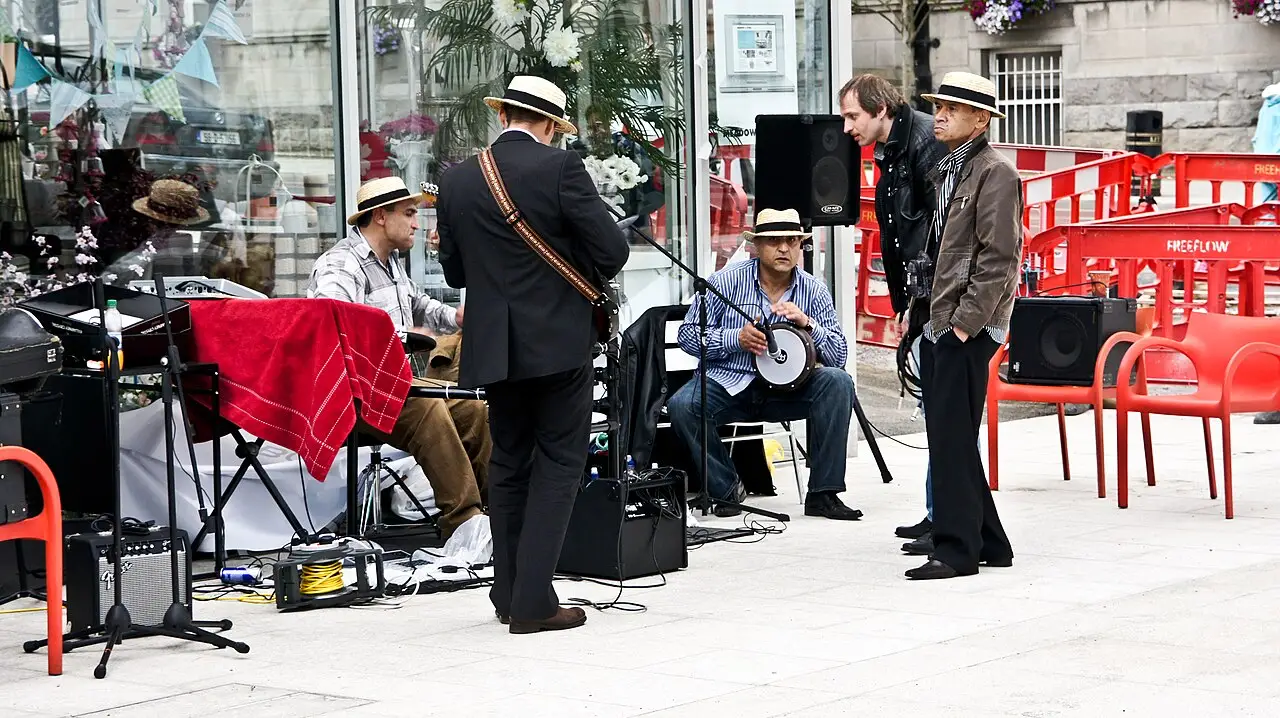 Músicos de chapéu de palha e paletó tocando diante de uma loja durante as comemorações do Bloomsday em Dún Laoghaire, em 2011, com passantes ao redor.