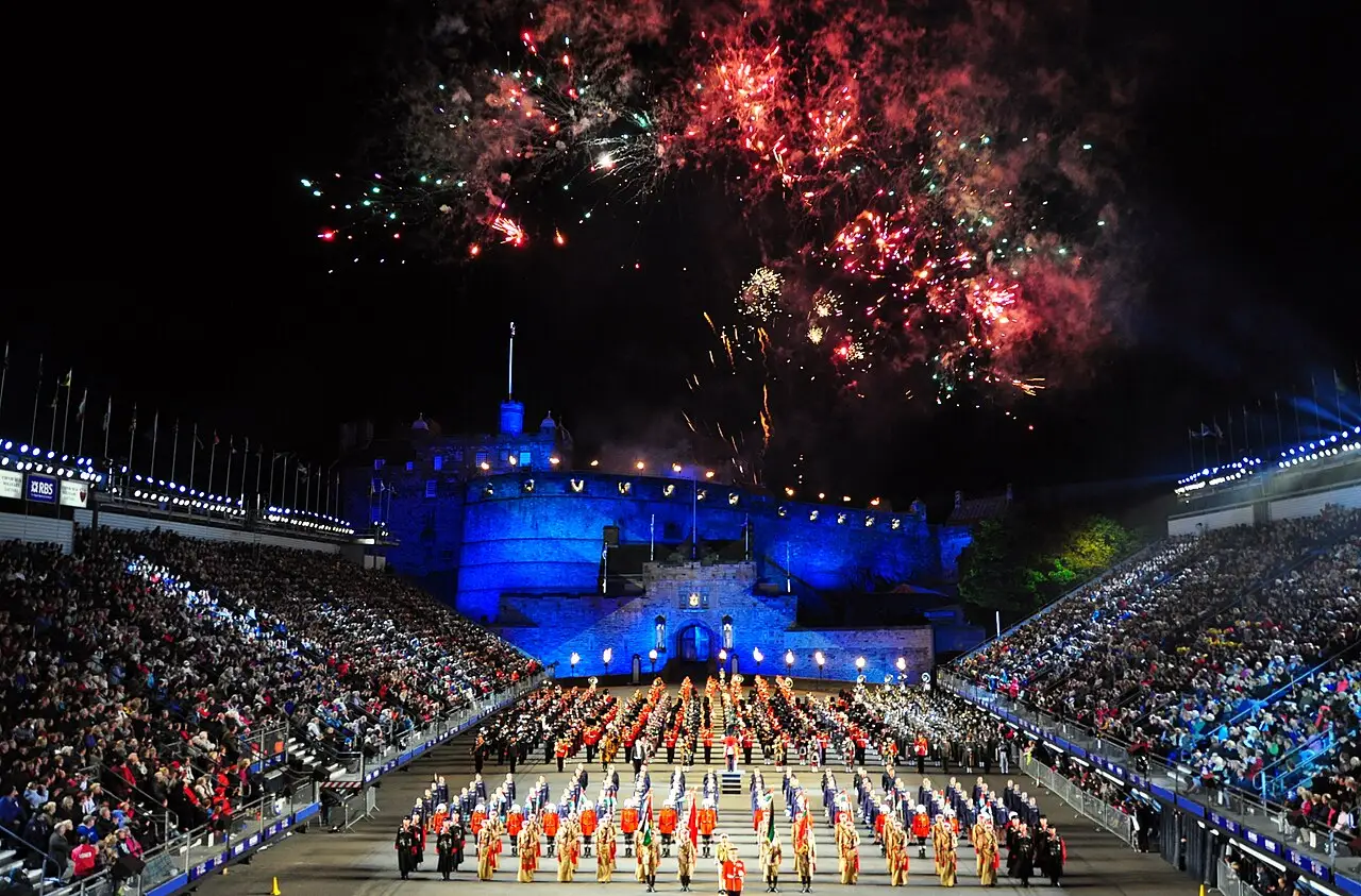 Esplanada do Castelo de Edimburgo iluminada em azul, com arquibancadas lotadas, bandas em formação e fogos de artifício no céu, em 2010.