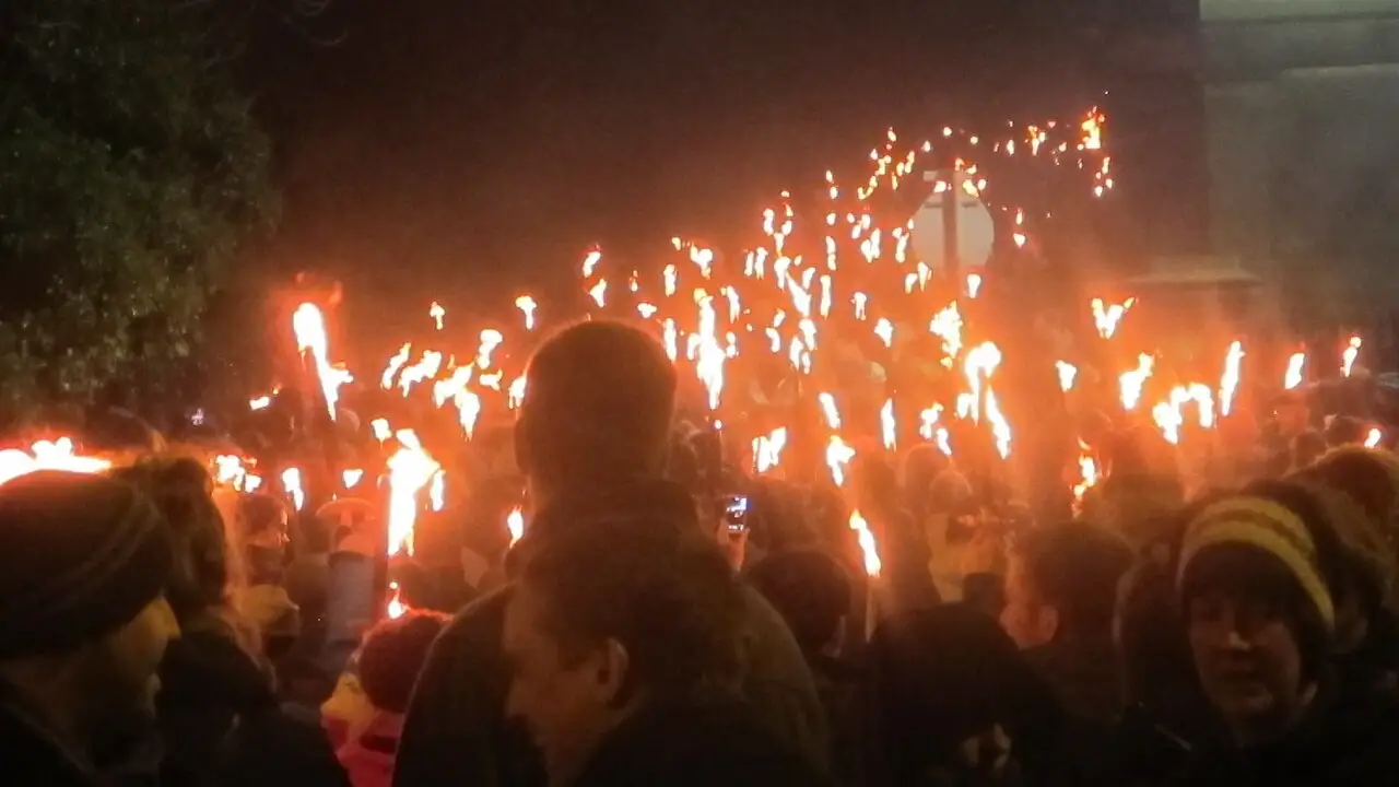Multidão de pessoas agasalhadas carregando tochas acesas em fila, à noite, durante o desfile de tochas do Hogmanay em Edimburgo.