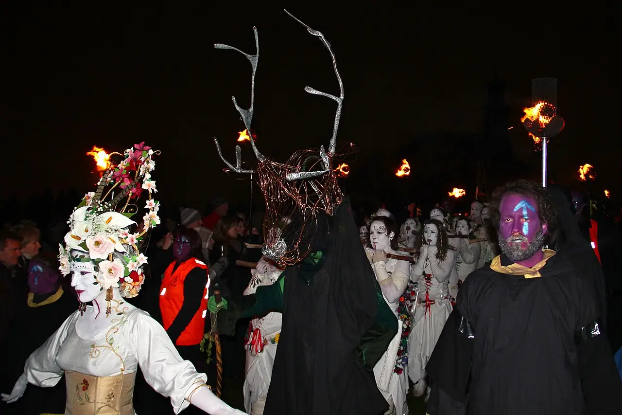 Figuras com máscaras brancas, capas escuras e chifres, algumas com tochas, em procissão à noite durante o Beltane Fire Festival de 2012 em Edimburgo.