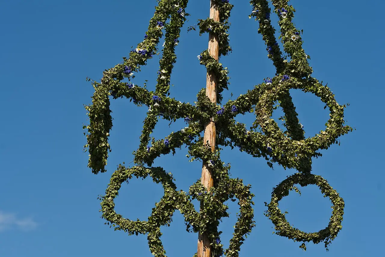 Mastro de Midsommar coberto de folhagem, com argolas de ramos, contra o céu azul no Skansen, em Estocolmo, em 2024.