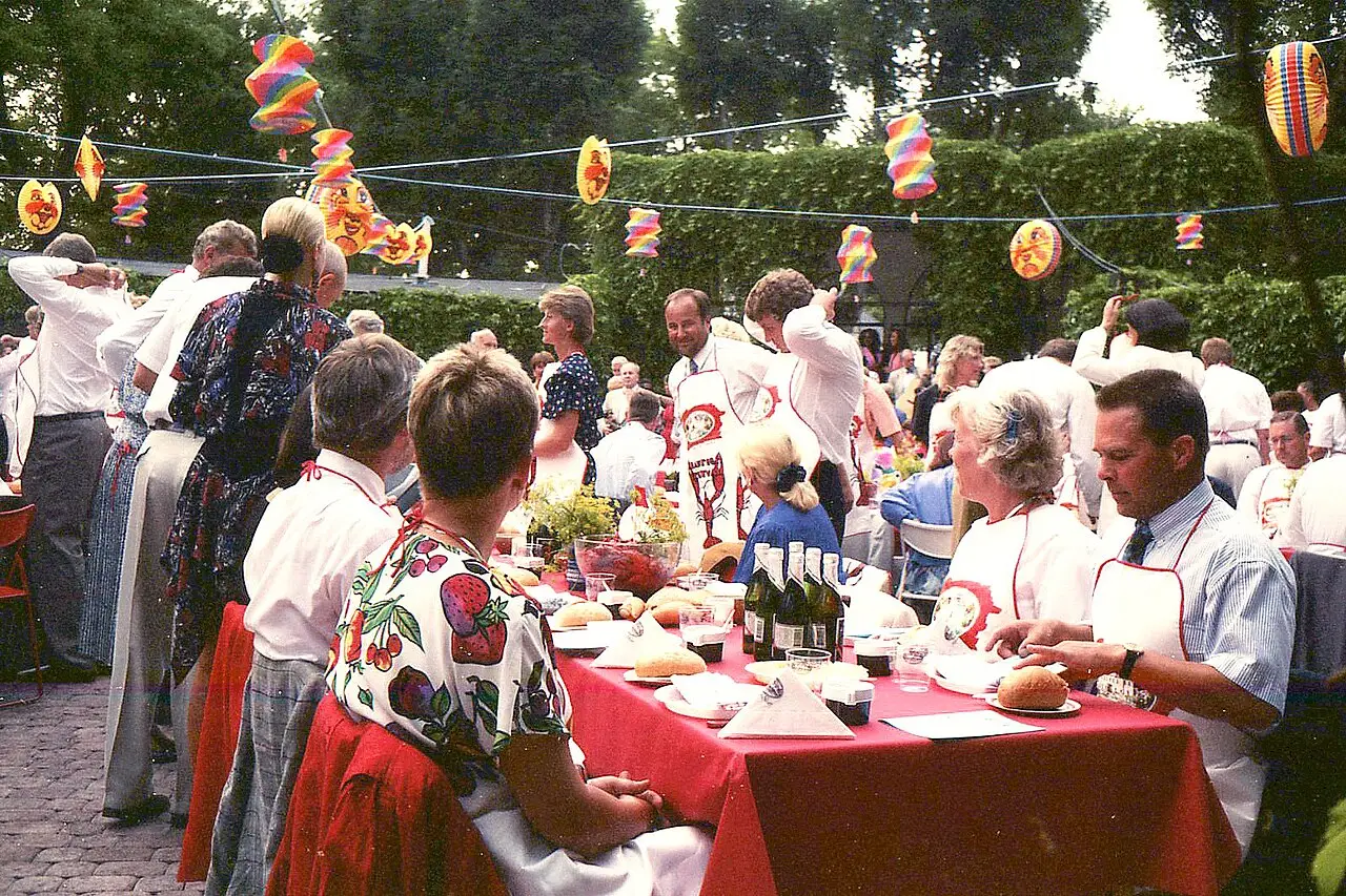 Convives attablés autour de tables aux nappes rouges, sous des lampions en papier suspendus aux arbres, lors d’une fête aux écrevisses en 1991.