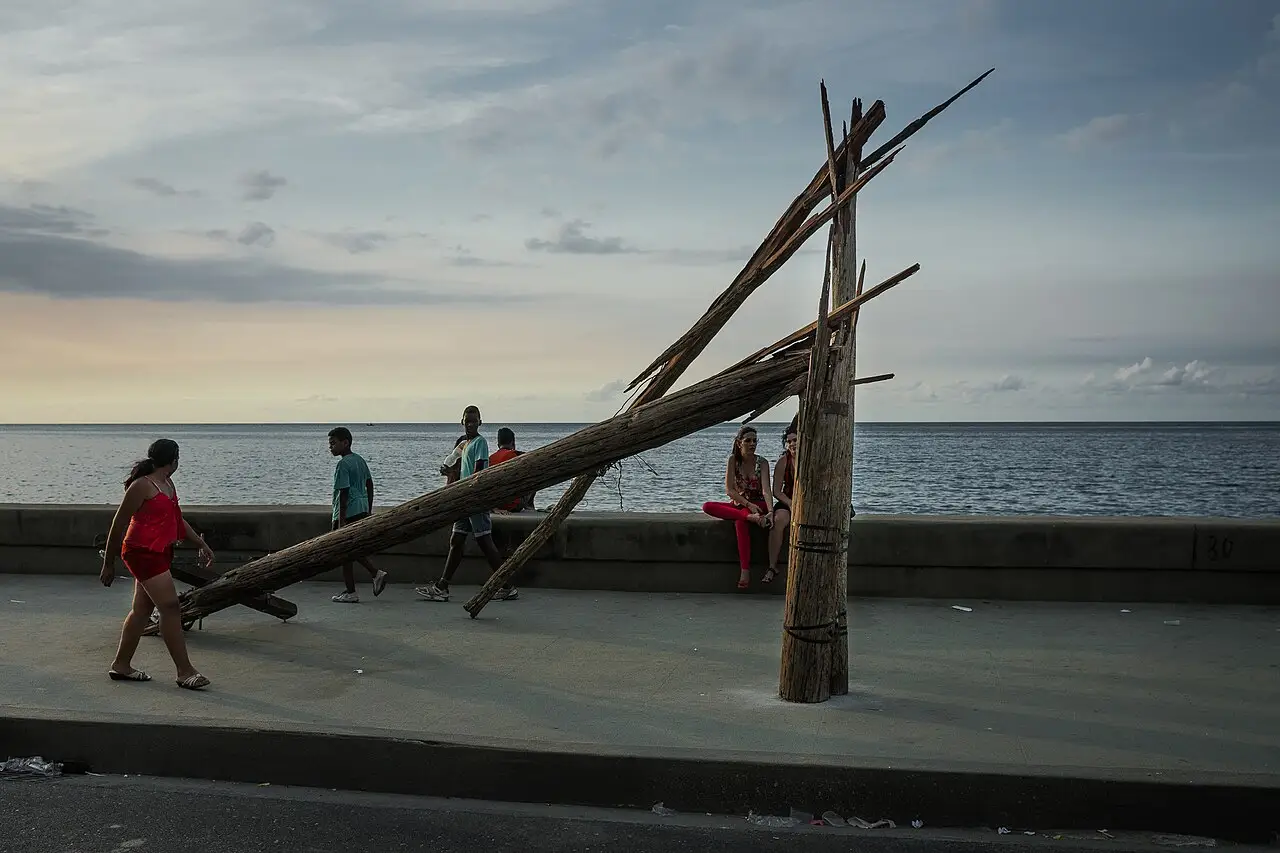 Estrutura de madeira inclinada instalada no calçadão do Malecón, com o mar ao fundo e pessoas passando, na Bienal de Havana de 2015.