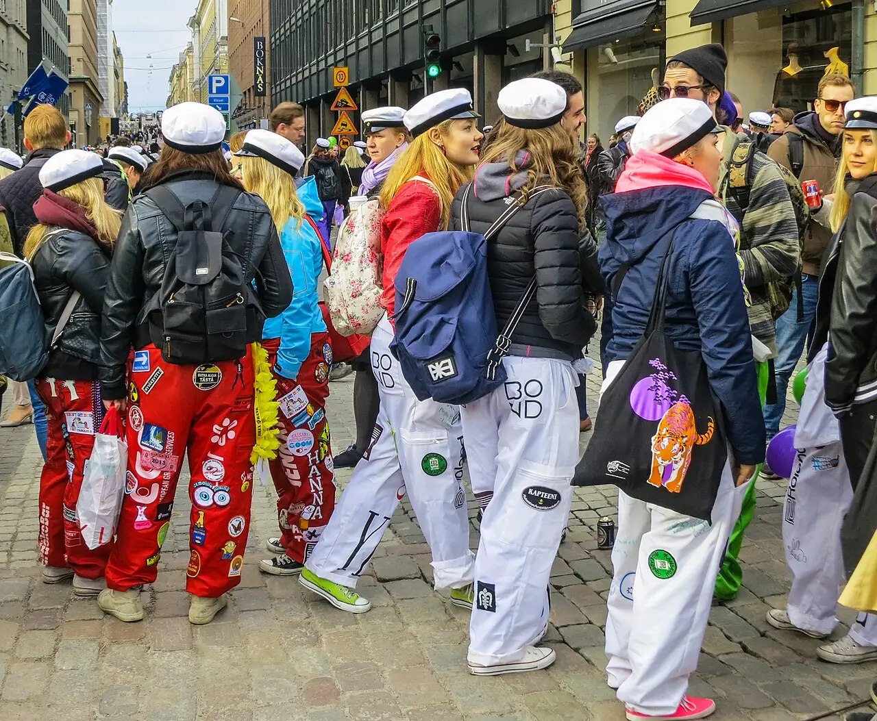 Estudantes finlandeses com bonés brancos e macacões coloridos cobertos de adesivos caminham numa rua de Helsinque na véspera do Vappu, em 2016.